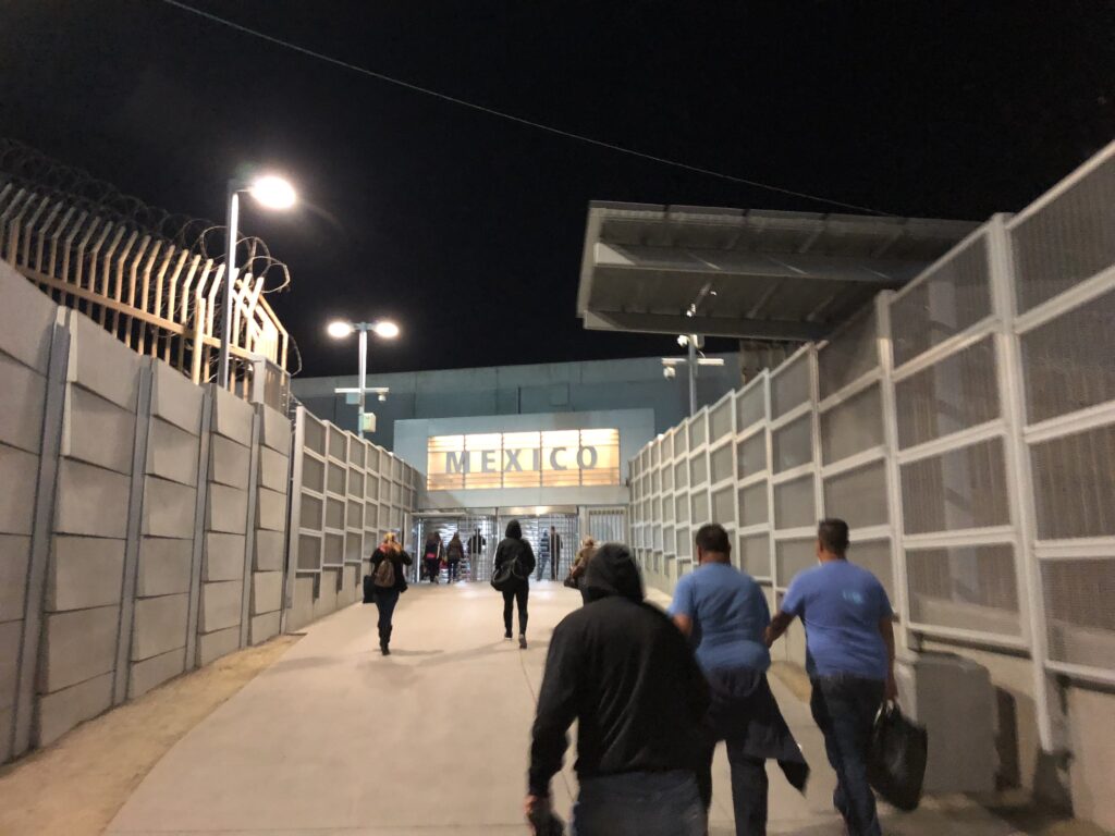 People walking through a border gate marked MEXICO (December 2017)