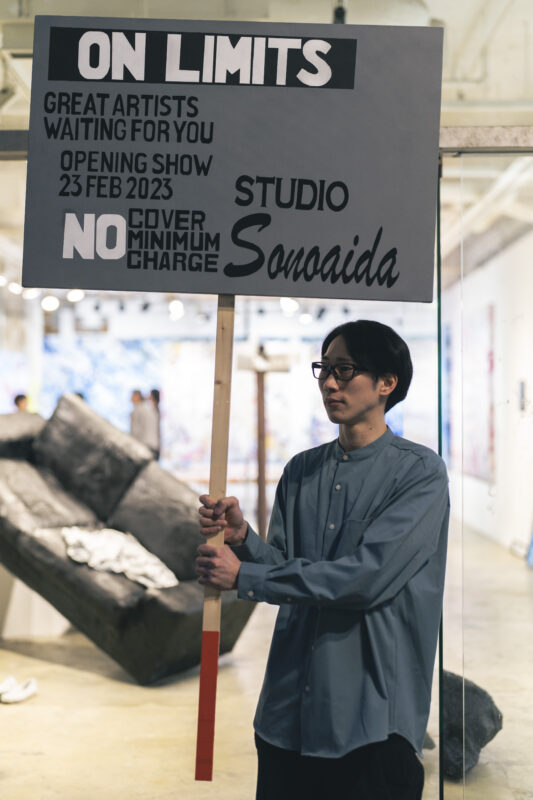 The sign ON LIMITS / OPENING SHOW 23 FEB 2023 / STUDIO Sonoaida, and Rui Yamaguchi carrying a tubular object (Sonoaida #Shin-Yurakucho, Tokyo)