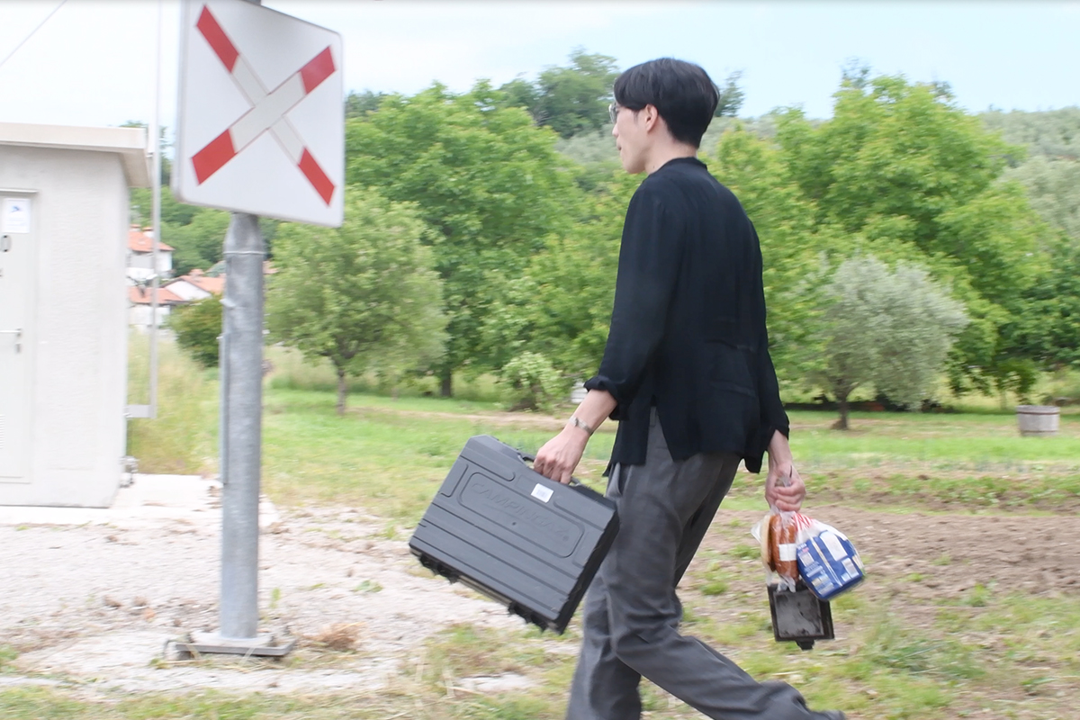 Rui Yamaguchi walking with his bags near the border along the railway tracks