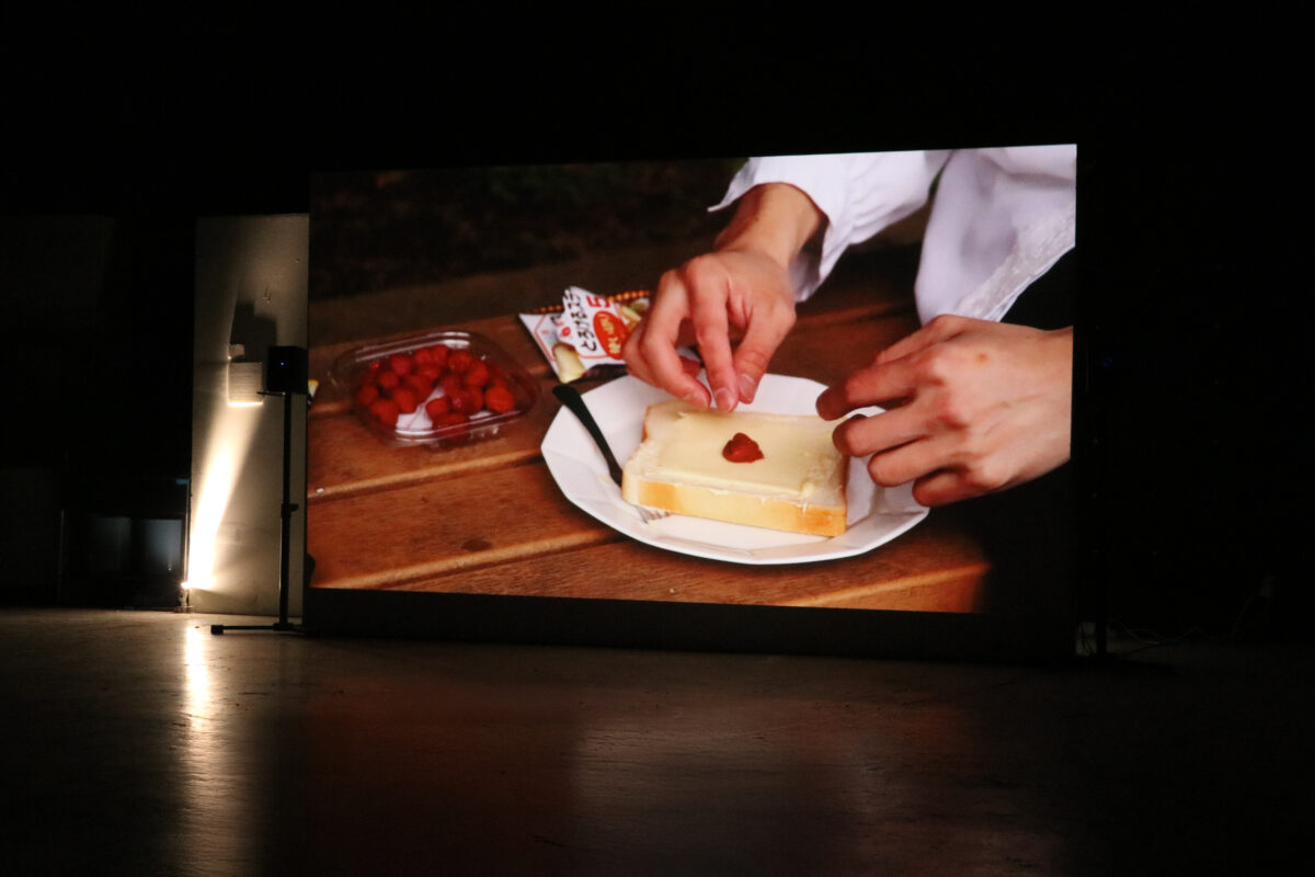 Eating Tour For Freedom #2 – installation view: the video showing a pickled plum being placed on white bread, screened in a dark exhibition space