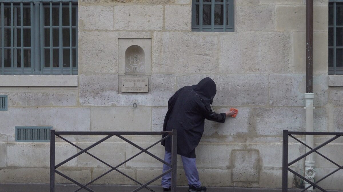 Demonstration for becoming a “professional unemployed” – the artist wiping the stone wall with an orange cloth in the rain, Rue de Seine, Paris