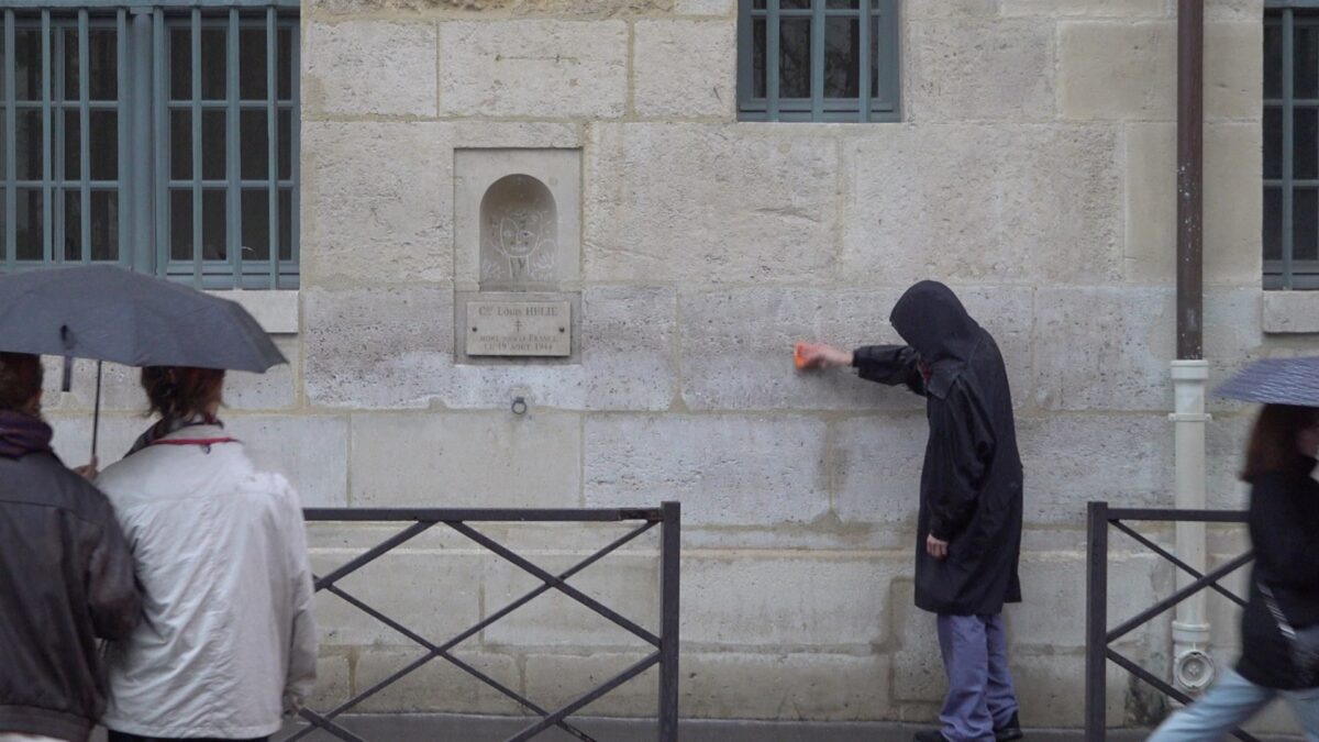 Demonstration for becoming a “professional unemployed” – the artist keeps wiping the wall as passersby with umbrellas walk by, Rue de Seine, Paris