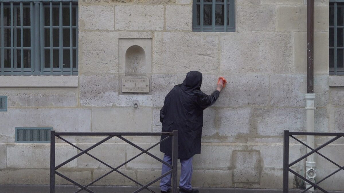 Demonstration for becoming a “professional unemployed” – the artist, seen from behind, wiping a high part of the wall with an orange cloth, Rue de Seine, Paris