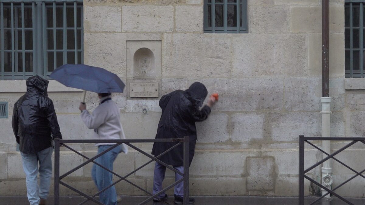 Demonstration for becoming a “professional unemployed” – the artist wiping the wall as a passerby with a blue umbrella walks past, Rue de Seine, Paris