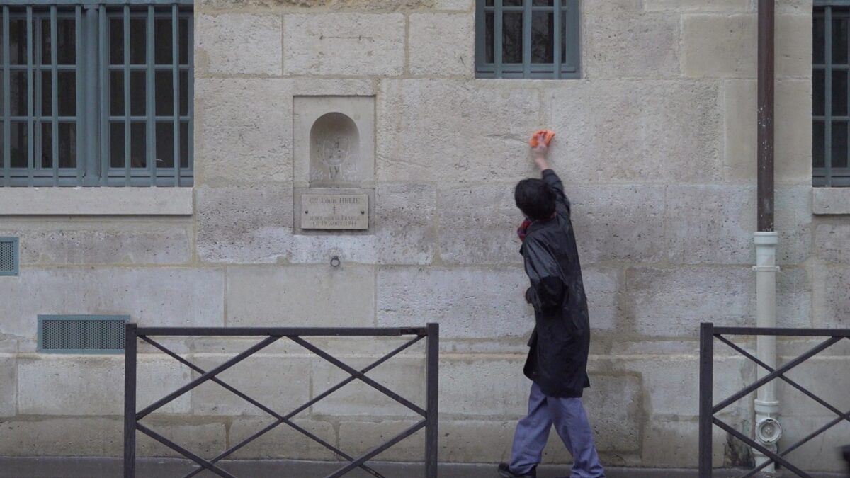 Demonstration for becoming a “professional unemployed” – the artist, hood down, stretching an arm to wipe the upper part of the wall, Rue de Seine, Paris